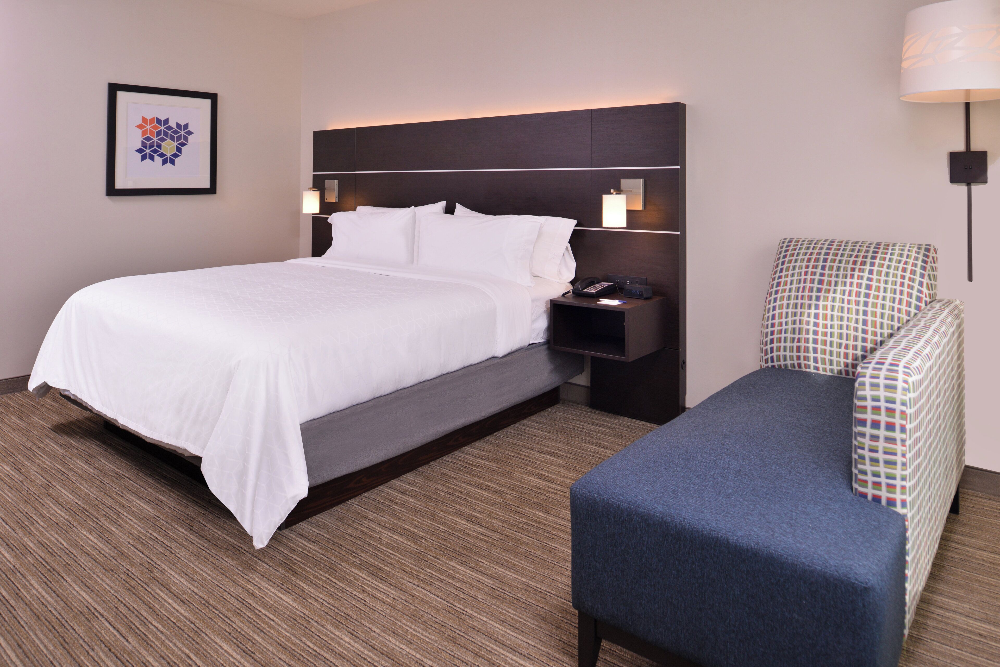 A hotel room with a bed, bedside table, lamp, and a chair.