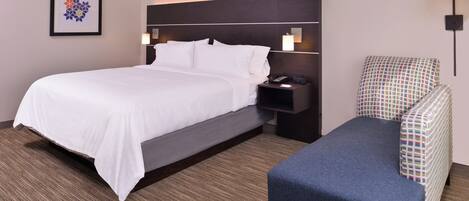 A hotel room with a bed, bedside table, lamp, and a chair.