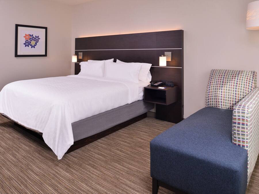 Una habitación de hotel con cama, mesita de noche, lámpara y una silla.
