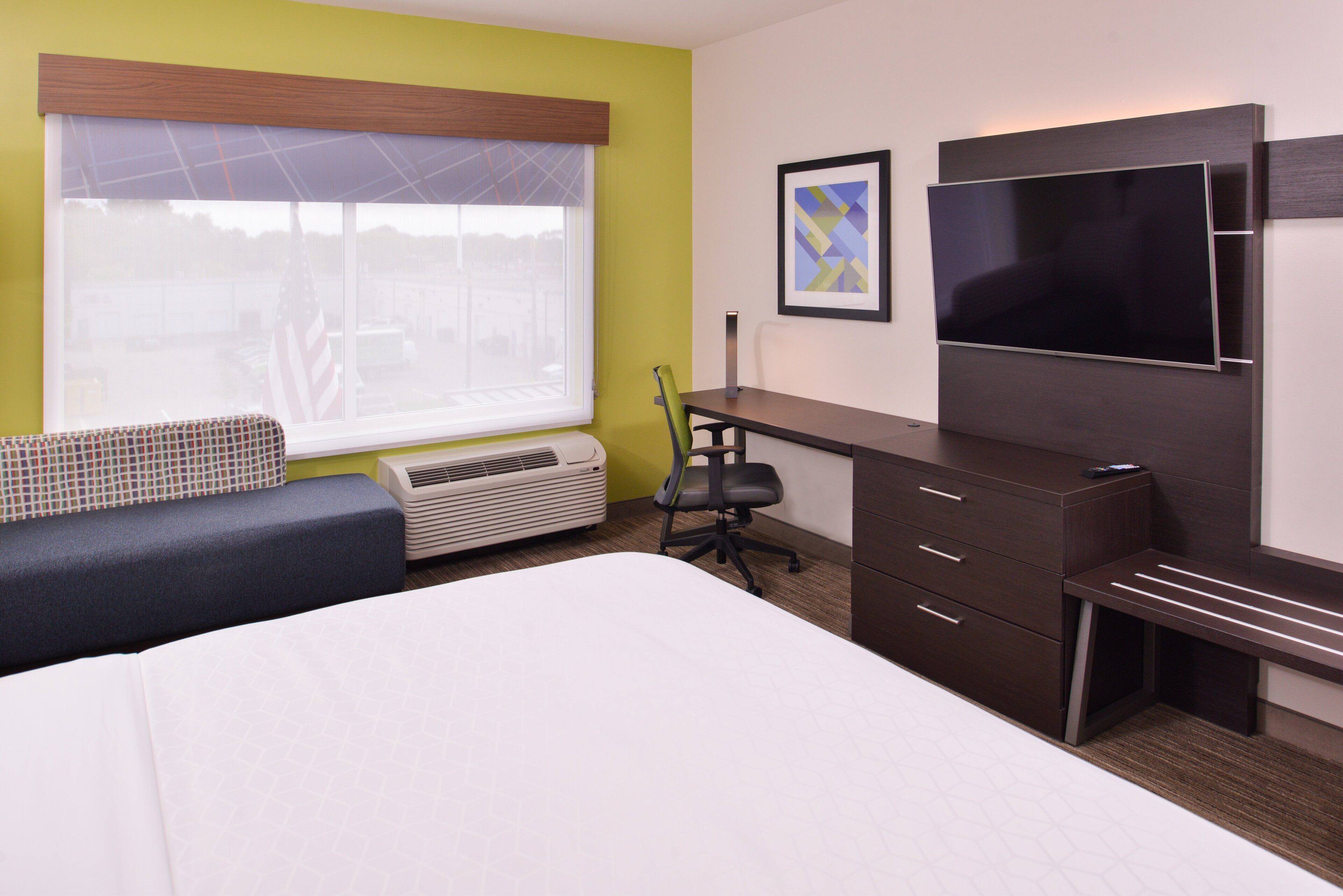 A hotel room with a bed, a desk, a chair, a TV, and a window with blinds.