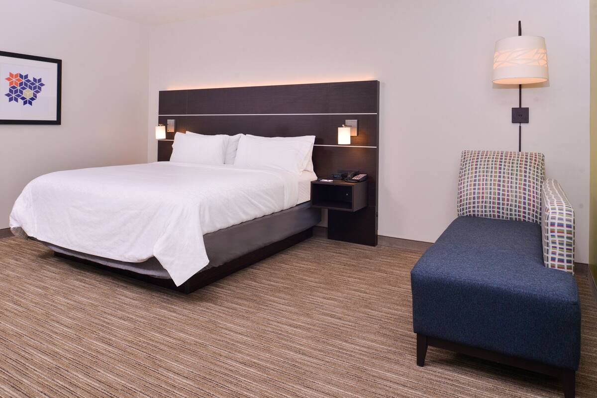 Een hotelkamer met een groot bed, een nachtkastje met een lamp en een gestreept fauteuil.