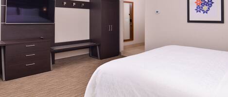 Una habitación de hotel con una cama grande, televisión, armario y una banca.
