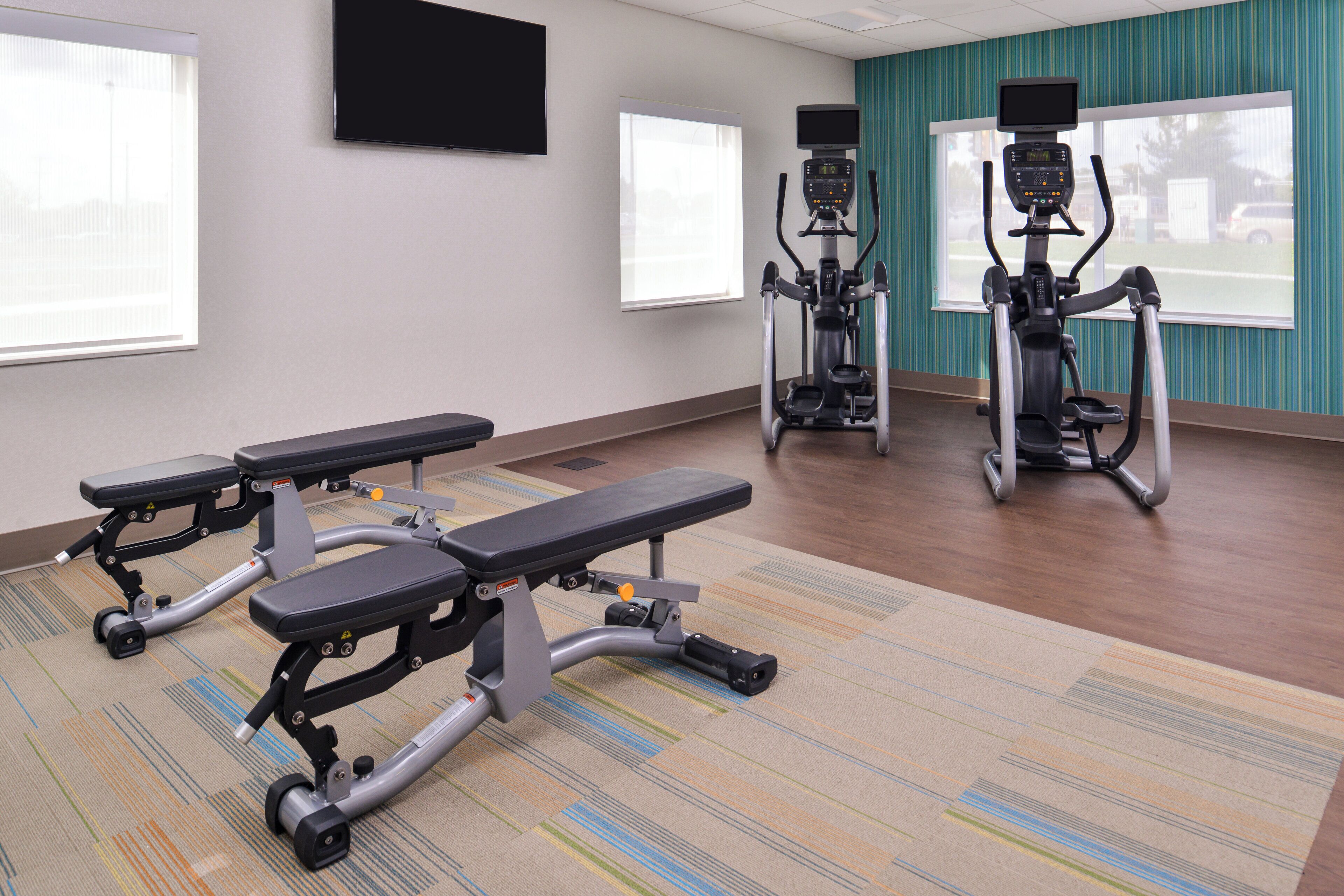A fitness room with treadmills, a bench, and a television on the wall.