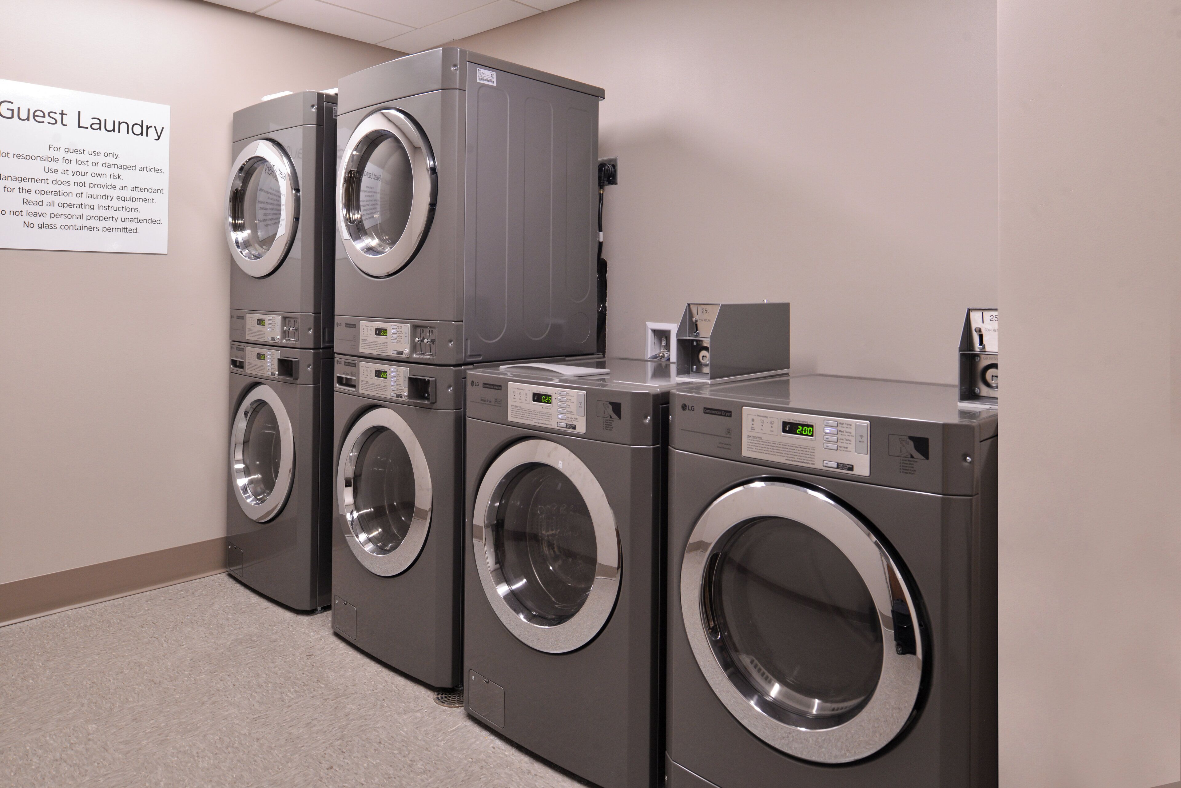Une rangée de quatre machines à laver et de quatre sèche-linge à chargement frontal, disposés les uns sur les autres, dans la buanderie d’un hôtel.