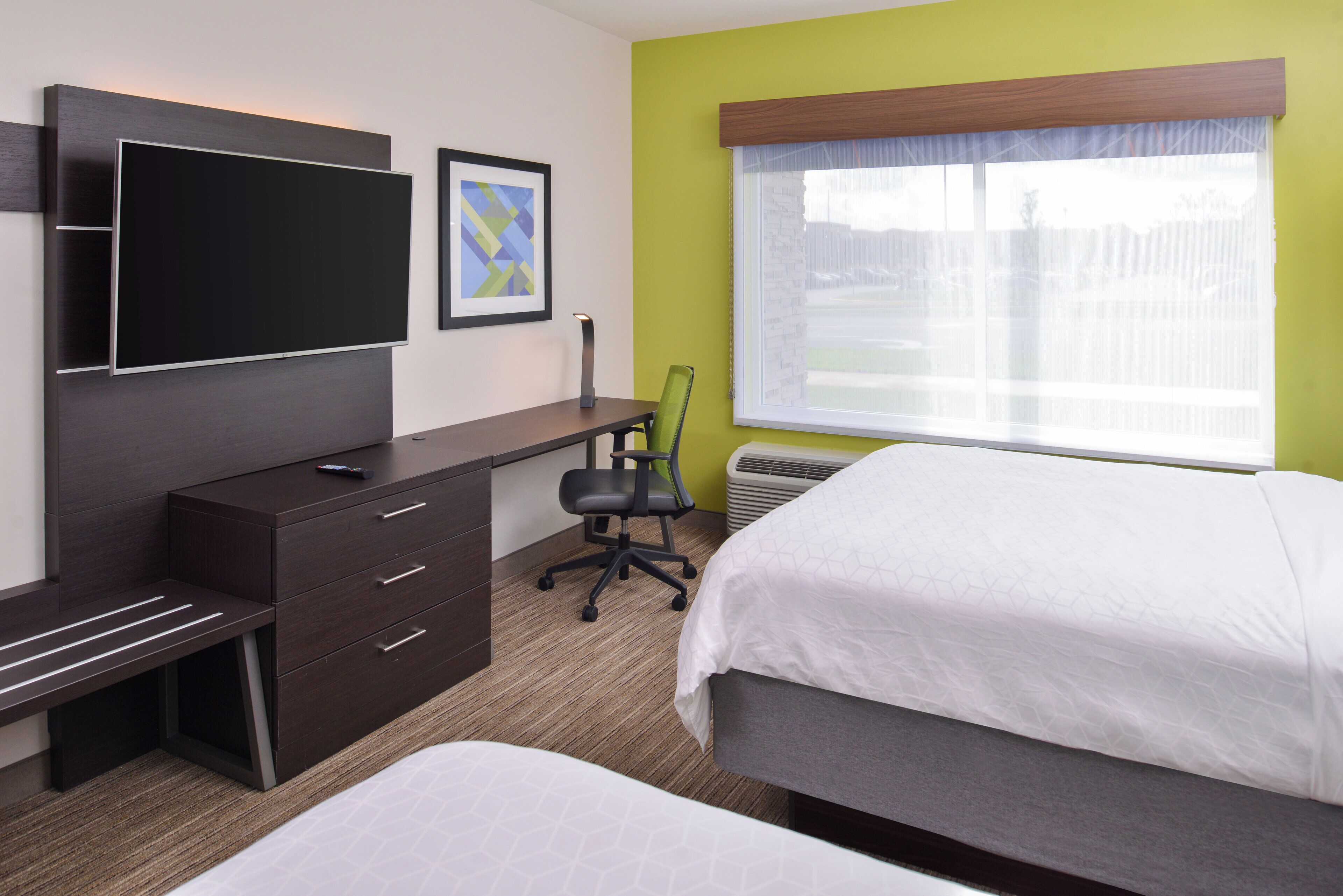 Een hotelkamer met een bed, een bureau met stoel, een televisie en een raam met uitzicht.