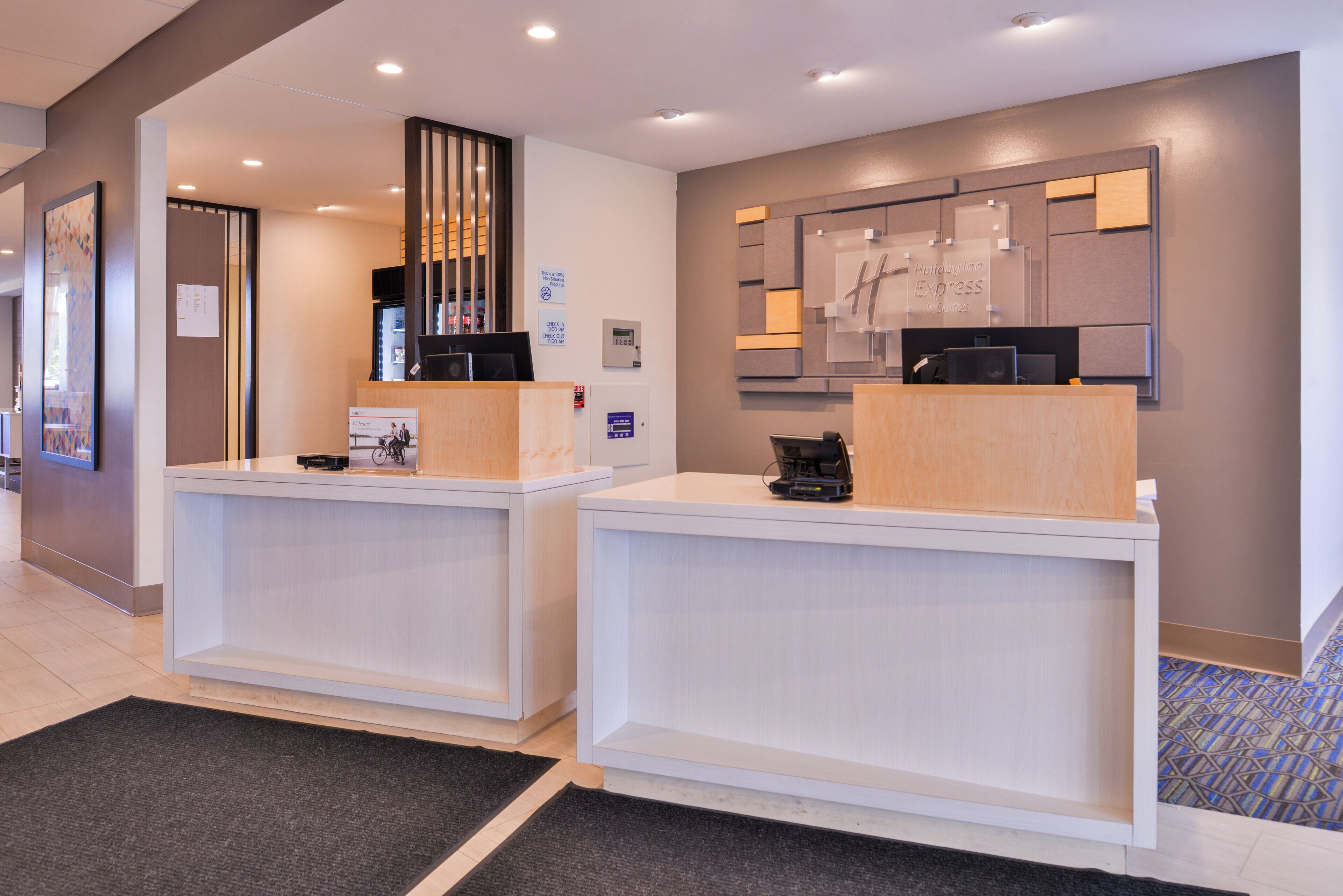 A reception desk with a digital screen, a fire alarm, and a sign indicating check-in times.