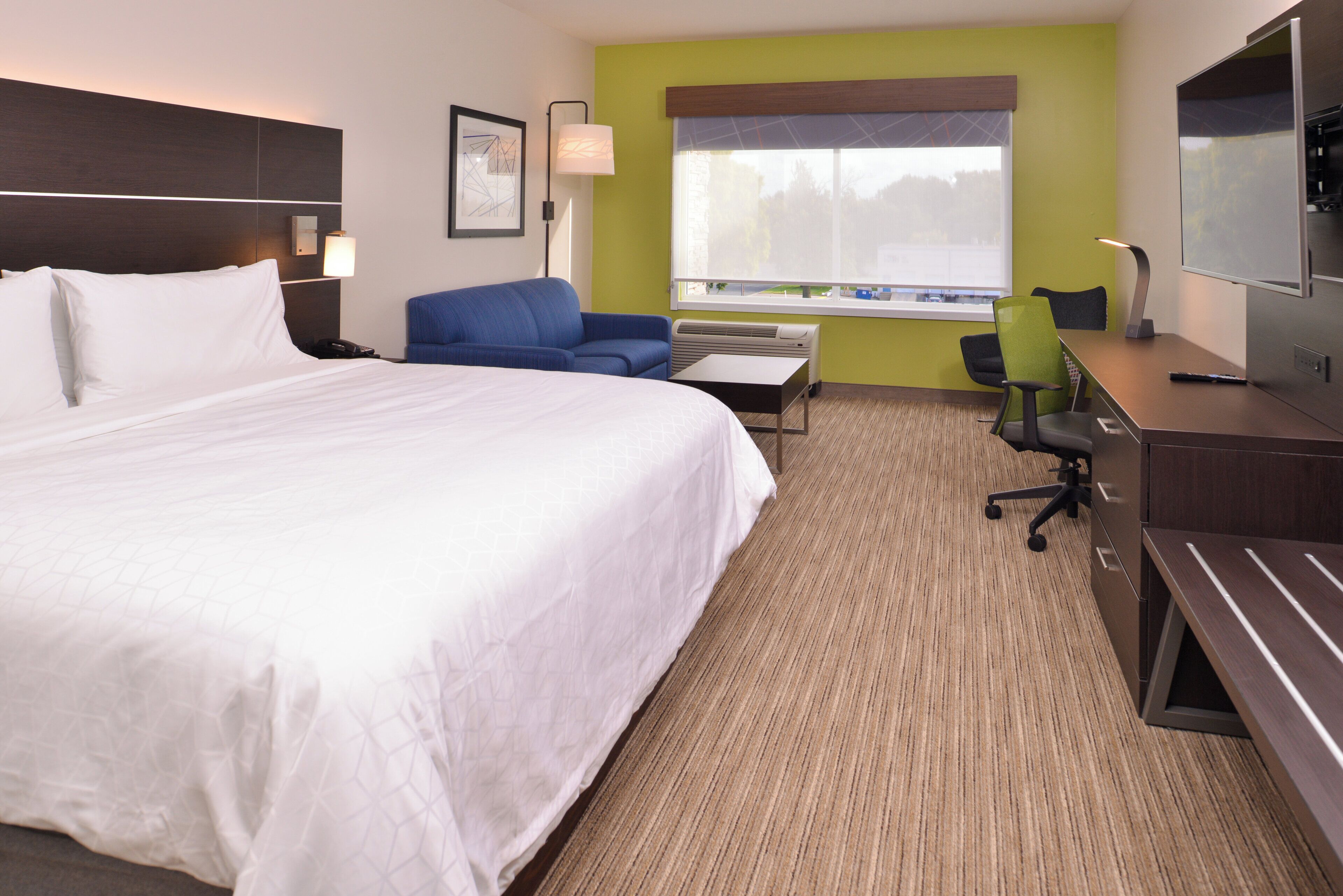A hotel room with a large bed, a desk, a chair, a television, and a window with a view.