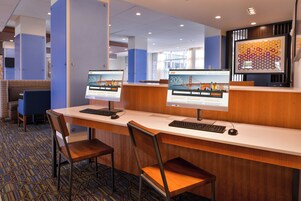 Zona de recepción de un hotel con dos monitores mostrando contenido promocional, un mostrador de recepción y un área de descanso con sillas.