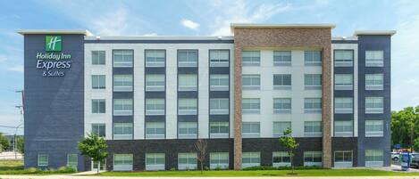 A Holiday Inn Express & Suites hotel building with a modern architectural design, featuring a mix of brick and stone facade, large windows, and a flat roof.