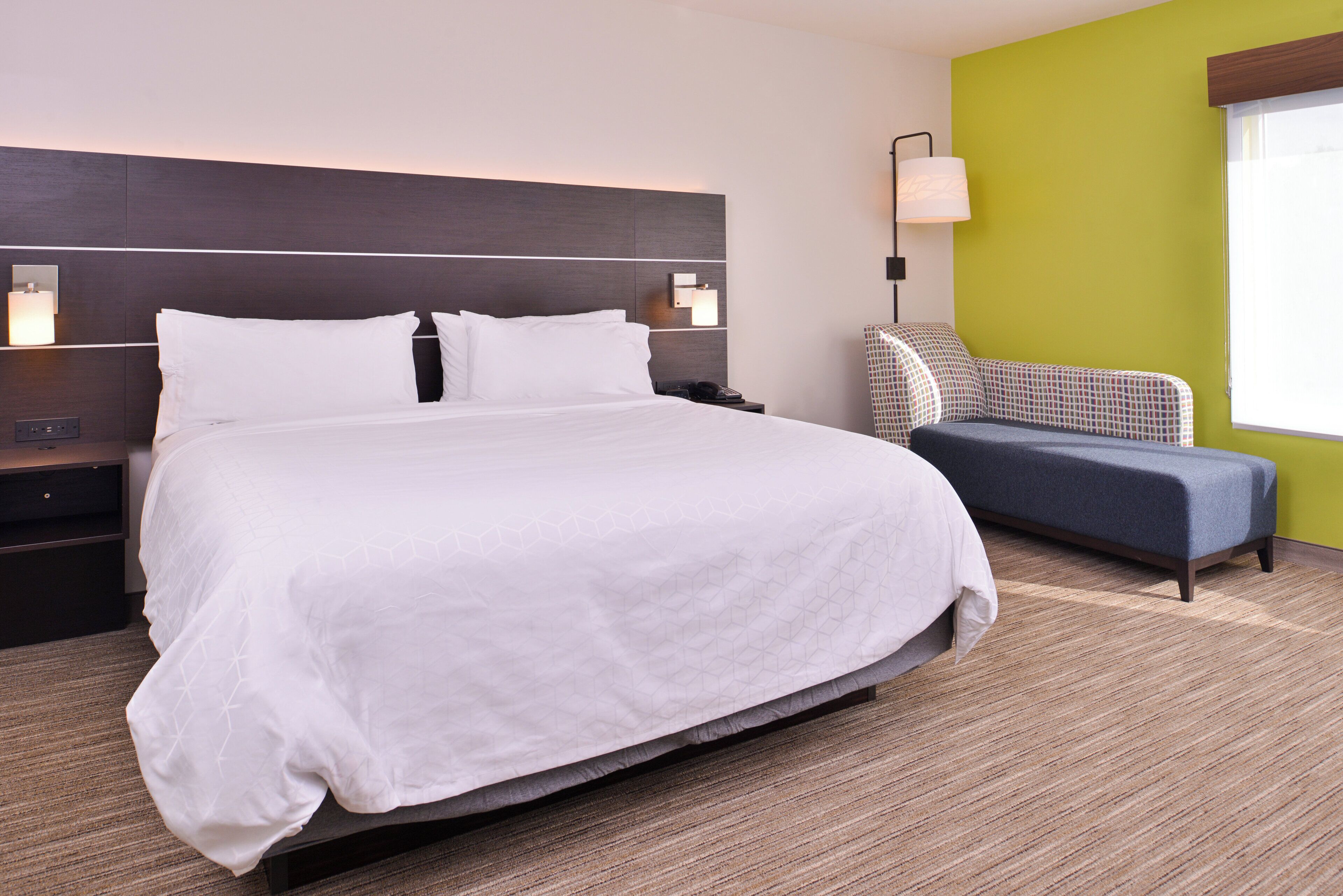 A hotel room with a large bed, bedside tables, a lamp, and a sofa.