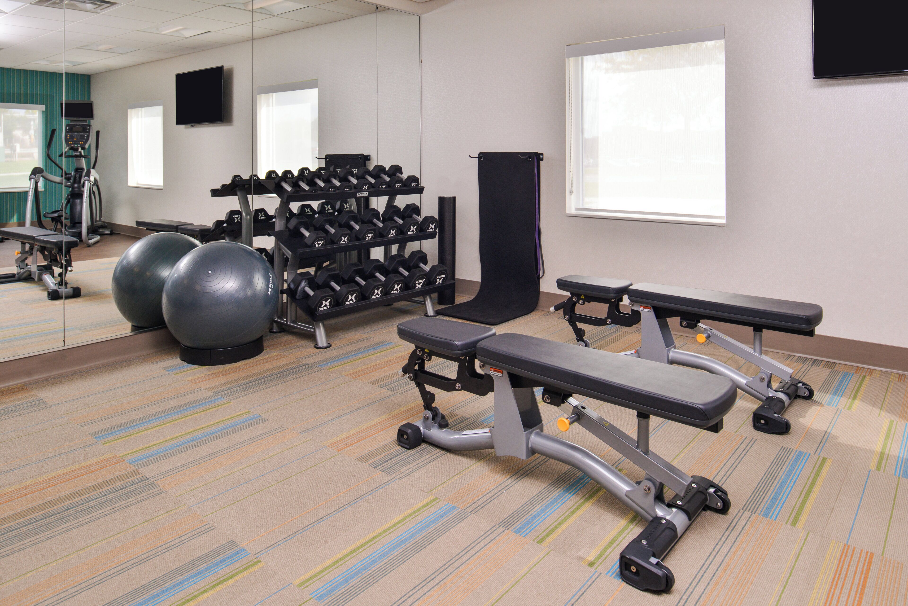 A gym with exercise equipment, a mirrored wall, and a window.