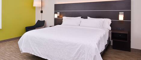 Una habitación de hotel con una cama grande, dos mesitas de noche, una silla y una lámpara de pared.