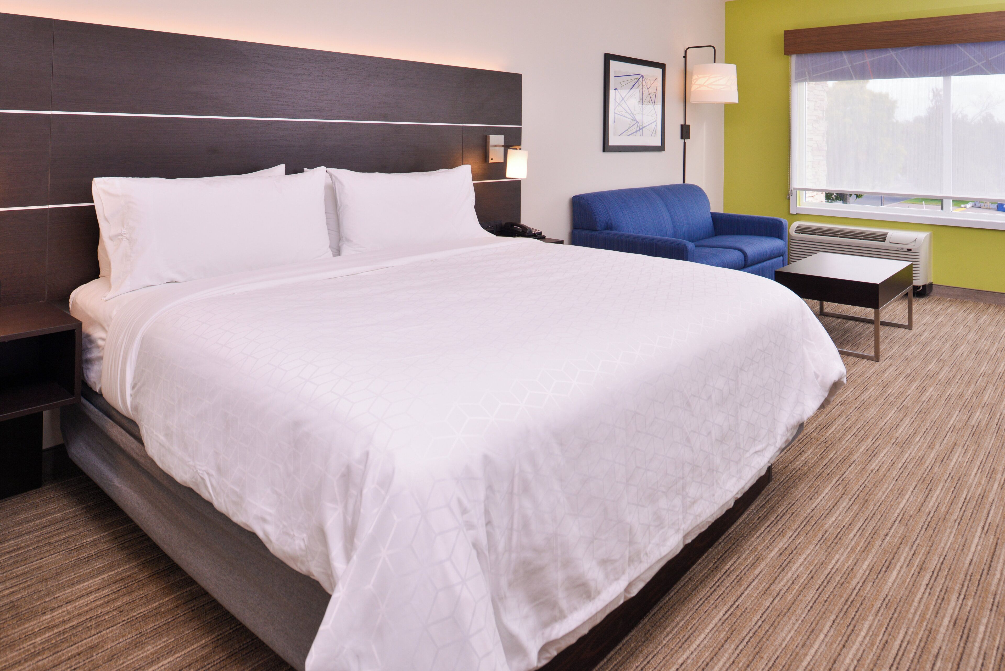 Quarto de hotel com uma cama grande, escrivaninha, cadeira e janela com vista.