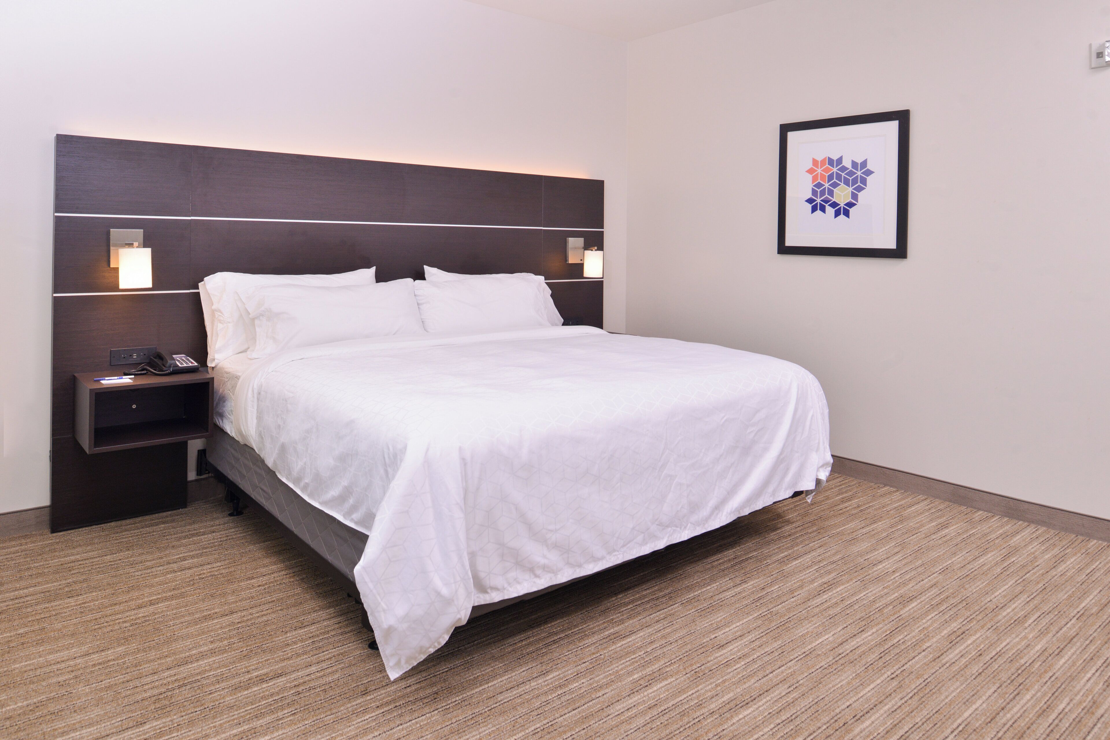 A hotel room with a bed, bedside tables, a phone, and a framed picture on the wall.