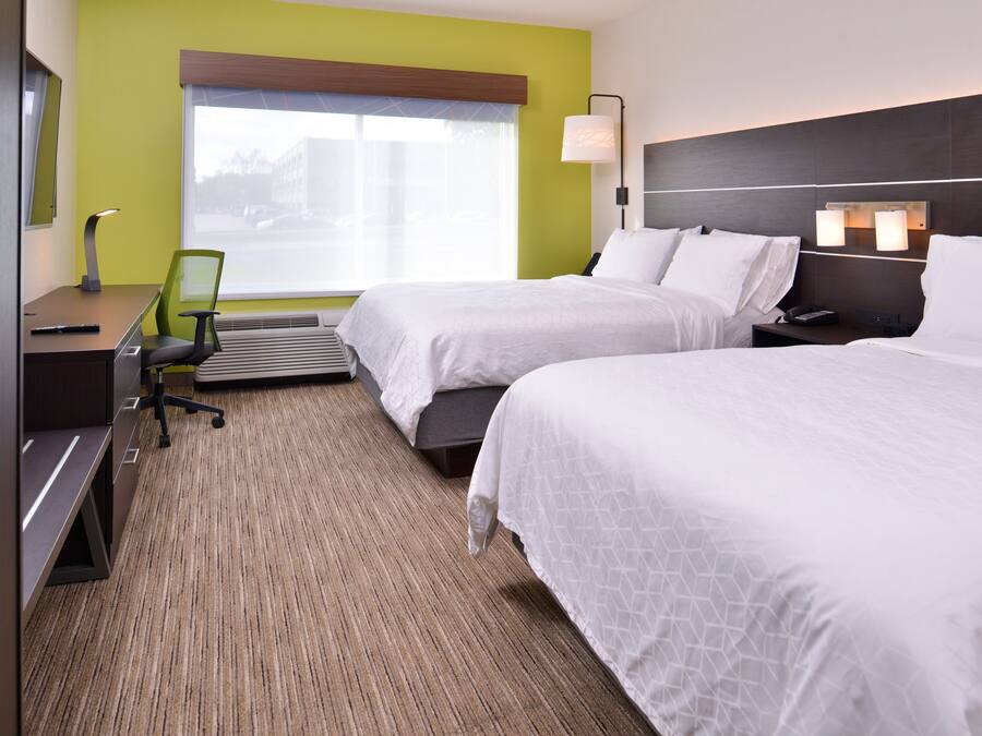A hotel room with two beds, a desk, a chair, and a large window.