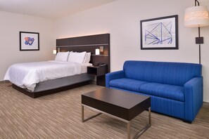 A hotel room with a bed, a blue sofa, a small table, and two wall-mounted lamps.