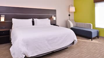 Una habitación de hotel con una cama grande, una mesita de noche, una lámpara y una silla.