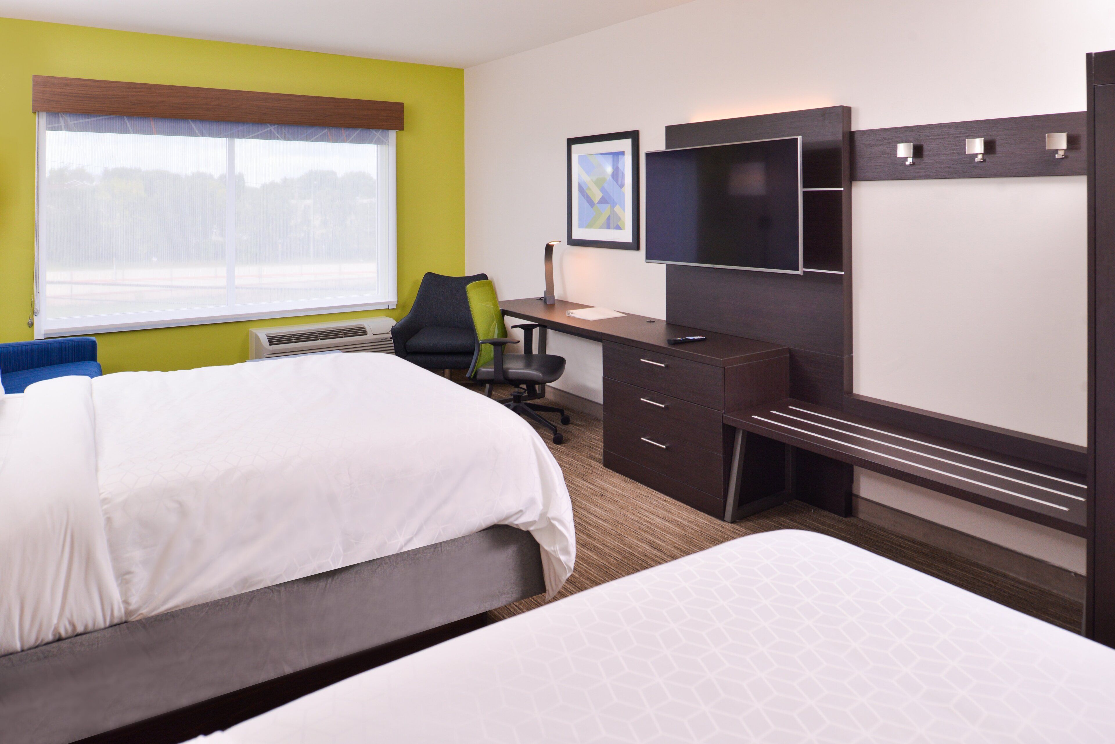 Una habitación de hotel con cama, escritorio, silla, televisor y ventana.
