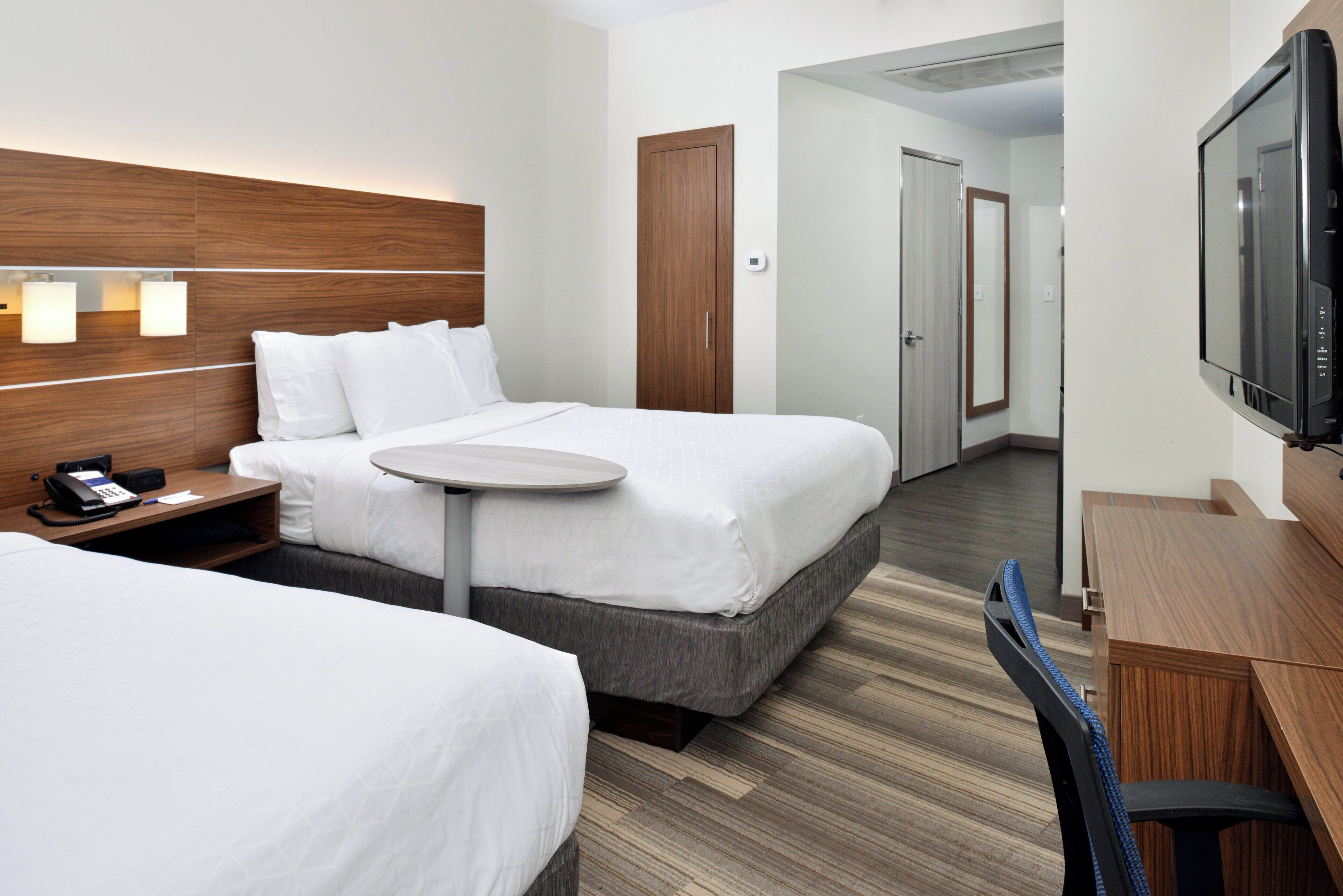 A hotel room with two beds, a desk with a telephone, a small table, a television, and a door leading to another room.
