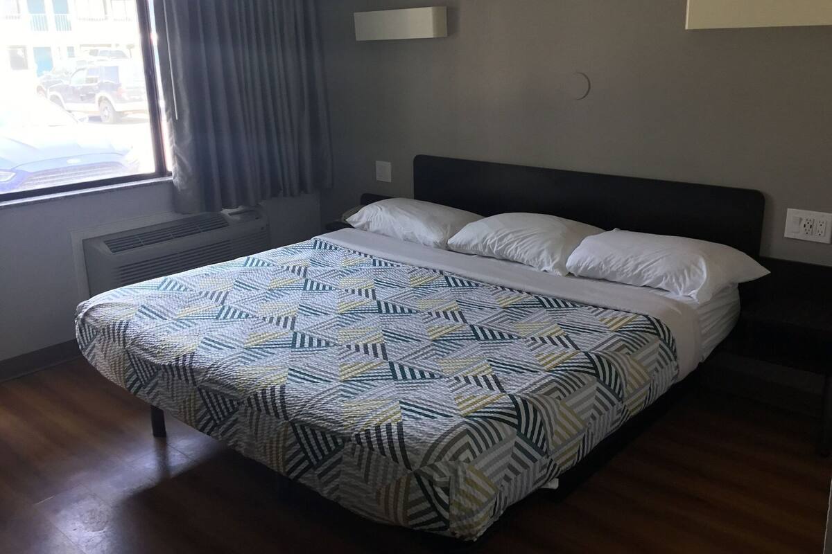 Quarto de hotel com cama, janela com cortinas, luminária na parede e tomada.