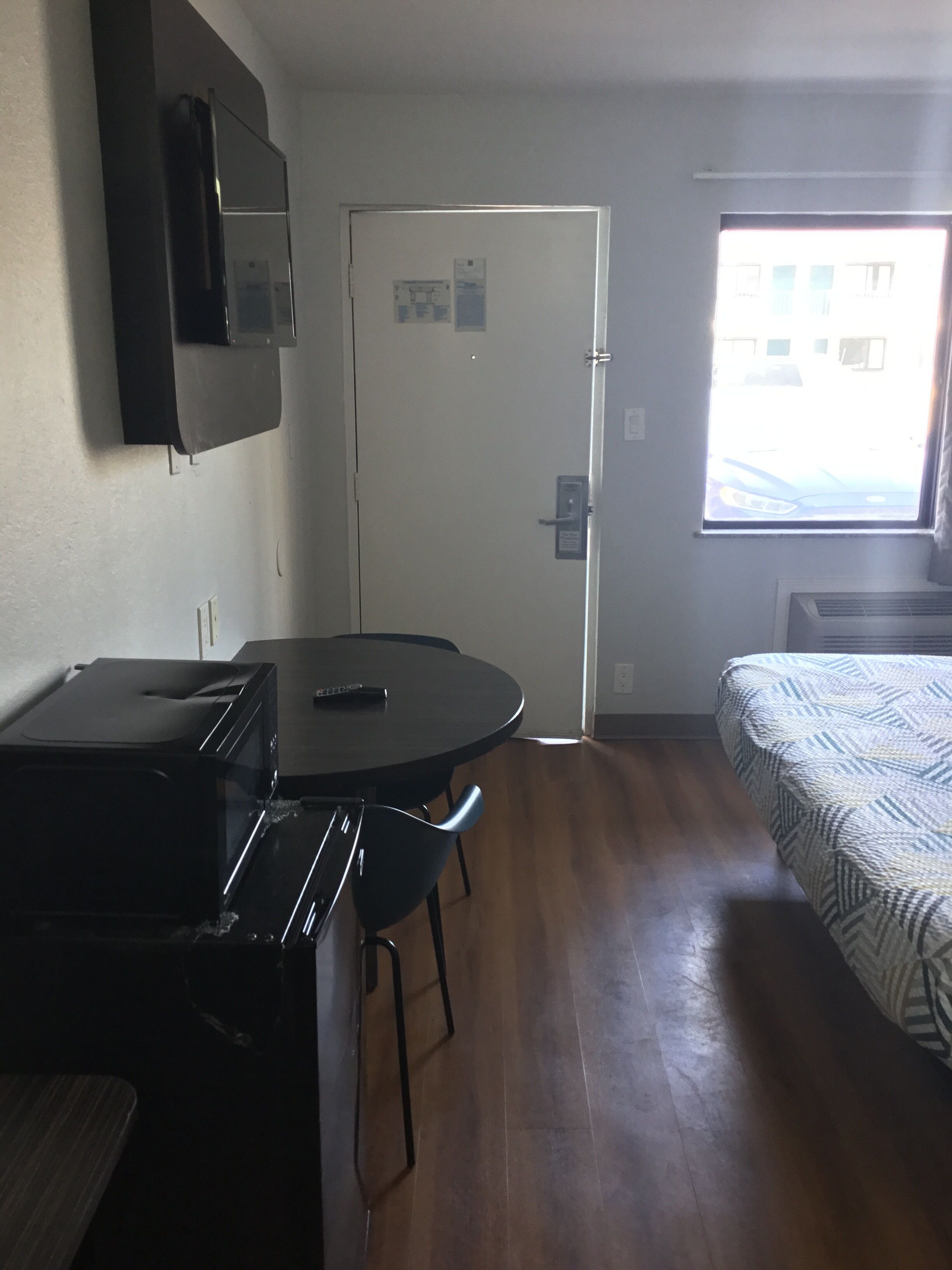 Una habitación compacta con kitchenette, una cama con ropa de cama estampada, una ventana con vistas y una puerta con cerradura.