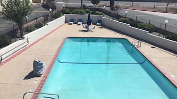 Una piscina rectangular con borde de azulejos, rodeada por un muro de ladrillo bajo y una barandilla metálica. Hay sillas de descanso y una mesita pequeña al borde de la piscina.