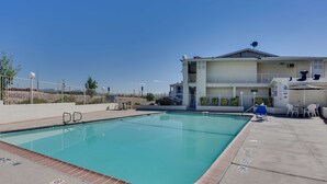 A swimming pool with a clear blue water, surrounded by a white fence, and a building with a balcony in the background. - Motel 6 El Paso, TX - West (El Paso)