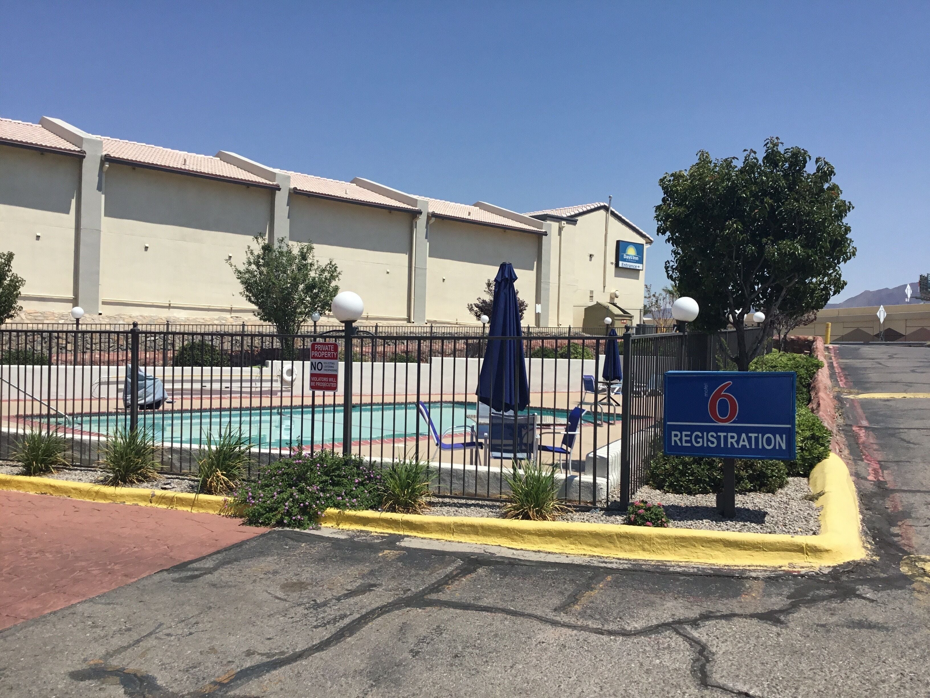 Un hotel con cartel de recepción, piscina y zona vallada con sillones de descanso.