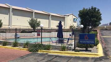 Un hotel con cartel de recepción, piscina y zona vallada con sillones de descanso.