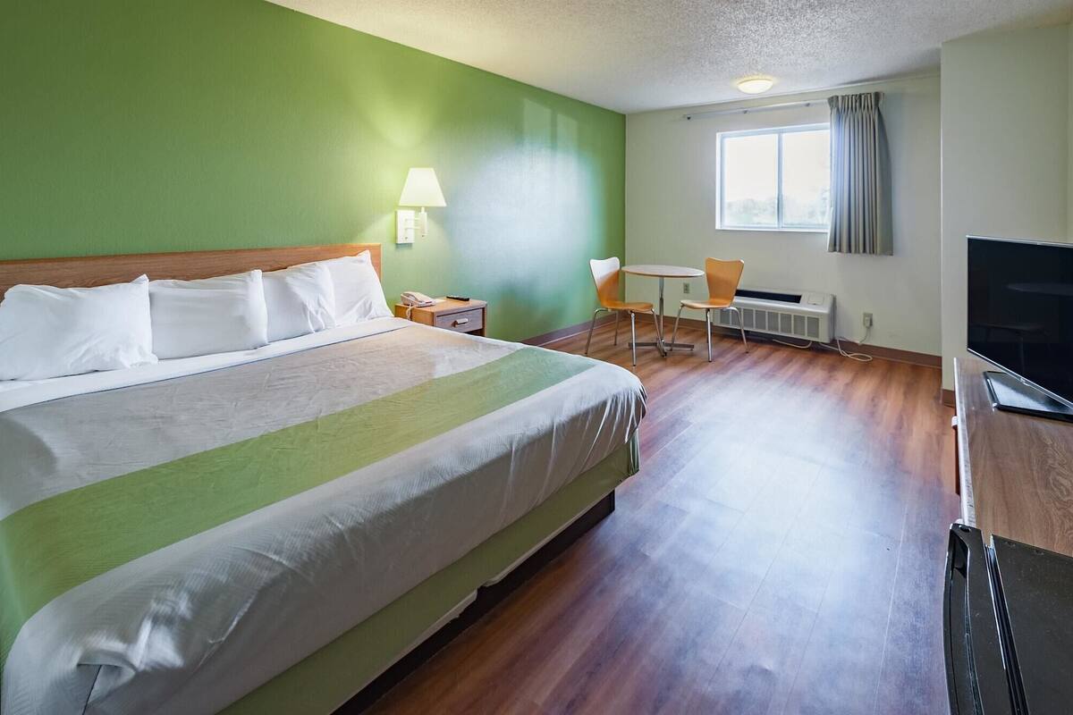 A hotel room with a large bed, a desk with a chair, a television, and a window with curtains.
