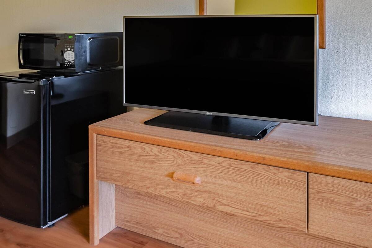 A kitchenette with a microwave, refrigerator, and a flat-screen TV on a wooden cabinet.