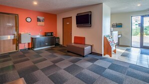 A hotel lobby with a check-in counter, a seating area, a clock, and a television. - Motel 6 Drums, PA (Drums)