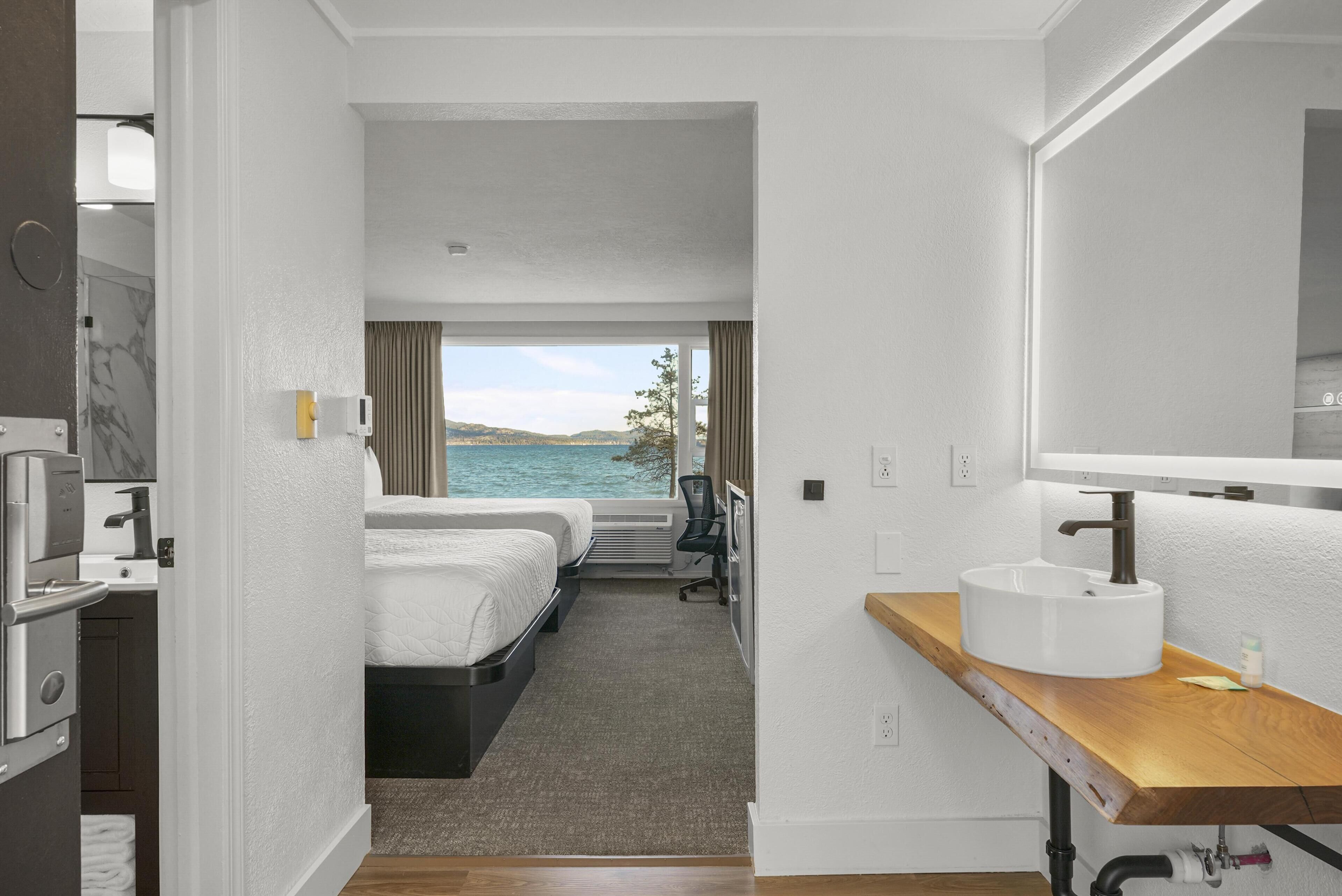 Ein Hotelzimmer mit Bett, Schreibtisch und einem Badezimmer mit Waschbecken, mit Blick auf das Meer.