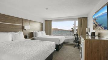 Habitación de hotel con dos camas, un escritorio, una silla y un amplio ventanal con vista al agua.
