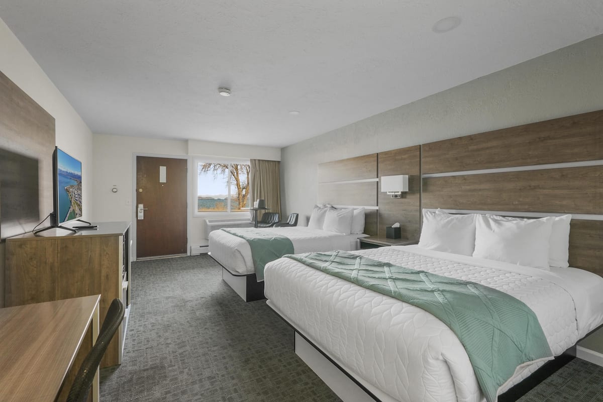 A hotel room with two beds, a desk, a TV, and a window with a view.