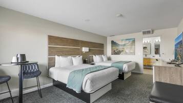 A hotel room with two beds, a desk, a chair, a small table, and a bathroom visible through an open door.