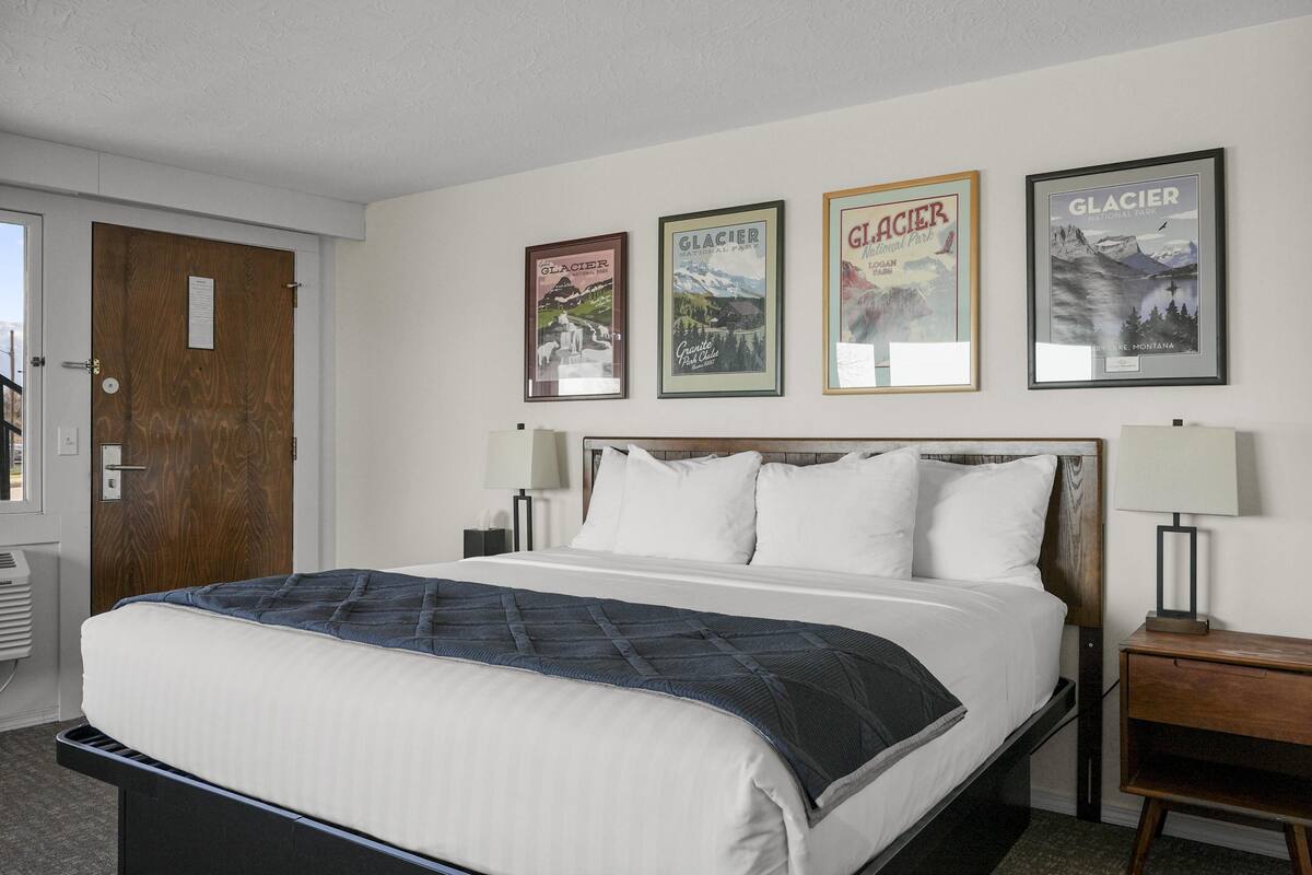 A hotel room with a bed, a wooden door, and three framed posters on the wall.