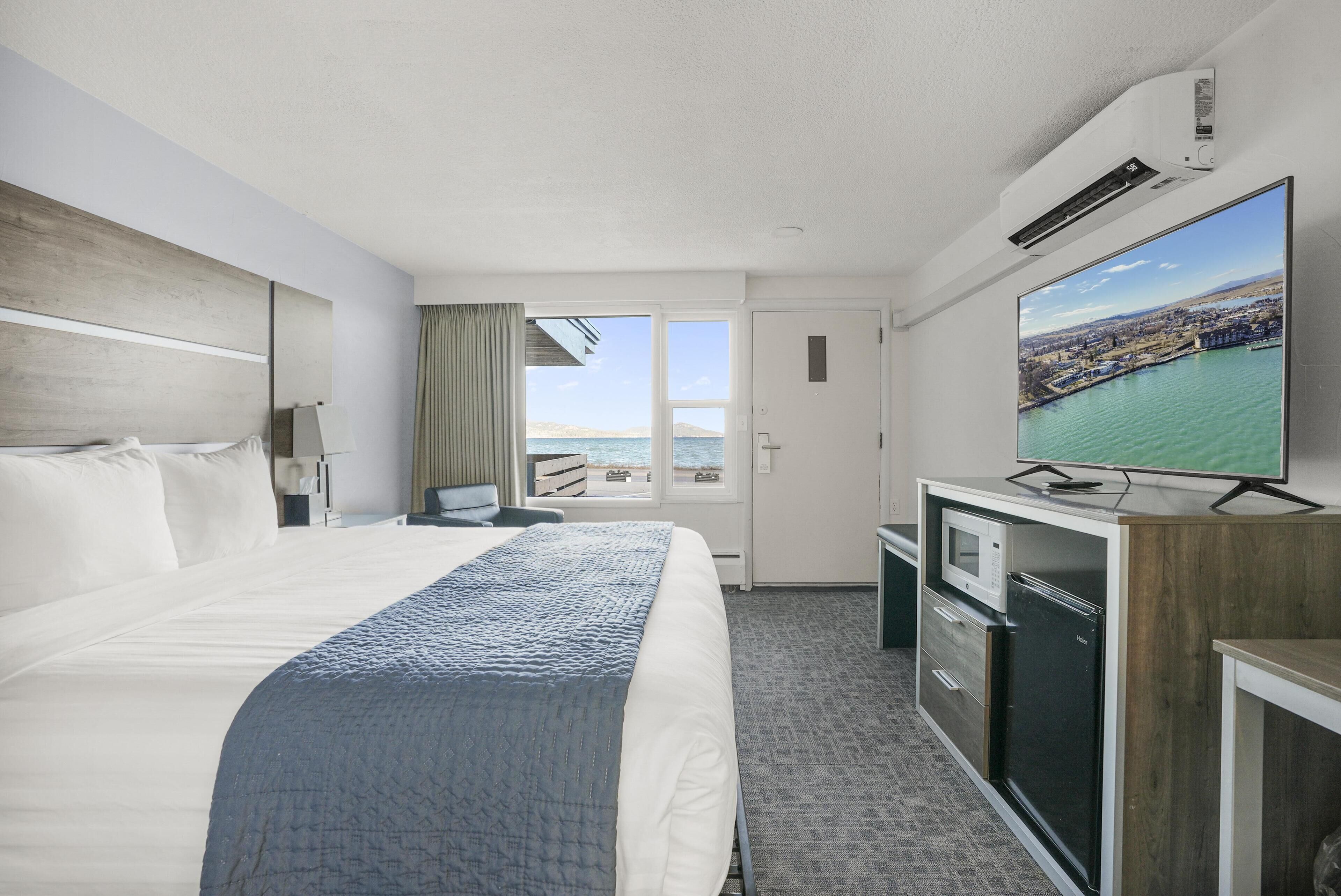 A hotel room with a large bed, a television, a desk with a microwave, and a view of the sea.