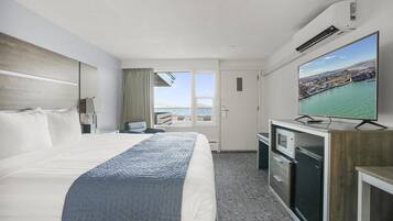 A hotel room with a large bed, a television, a desk with a microwave, and a view of the sea.