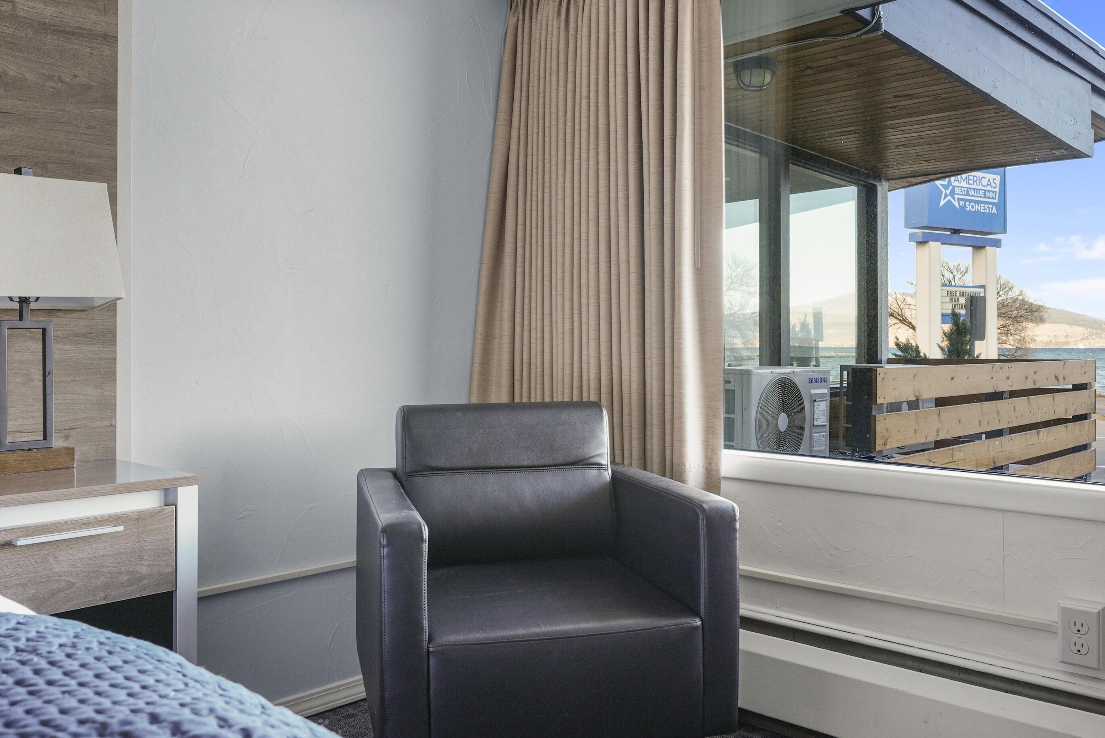 A hotel room with a large window, a chair, a desk, and a bed.