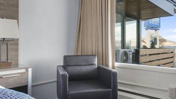 A hotel room with a large window, a chair, a desk, and a bed.