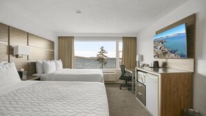 Habitación de hotel con dos camas, un escritorio, una silla, una kitchenette pequeña y un amplio ventanal con vistas al mar y las colinas.