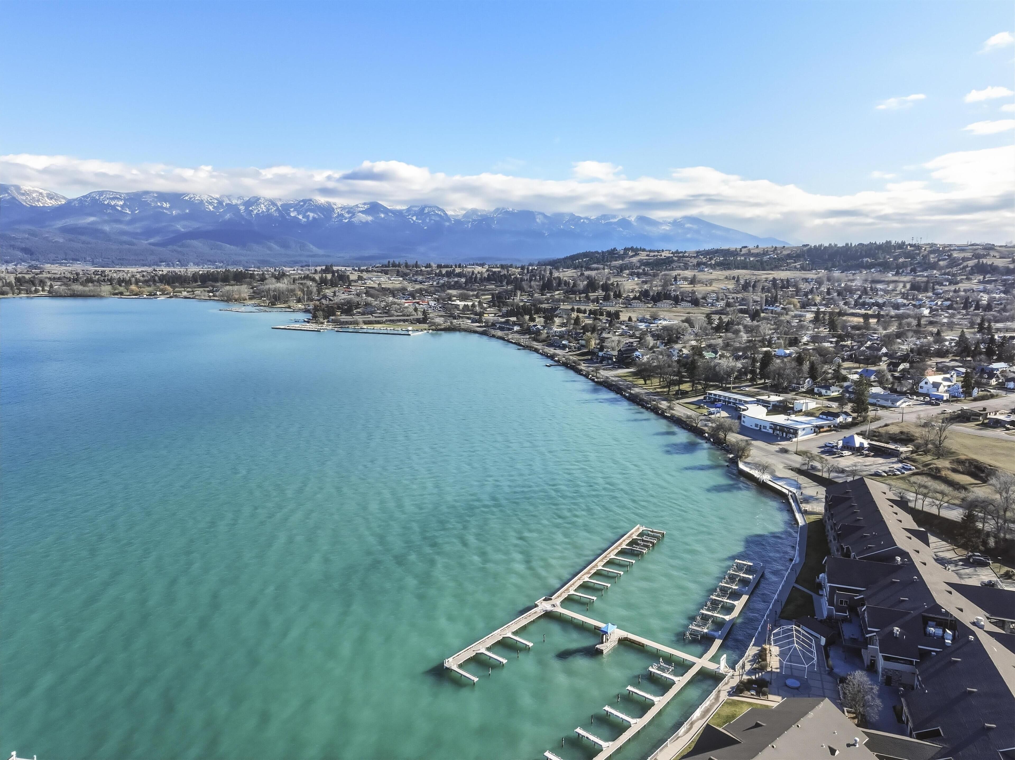 Vista aérea de un pueblo costero con un puerto deportivo, edificios residenciales y montañas al fondo.