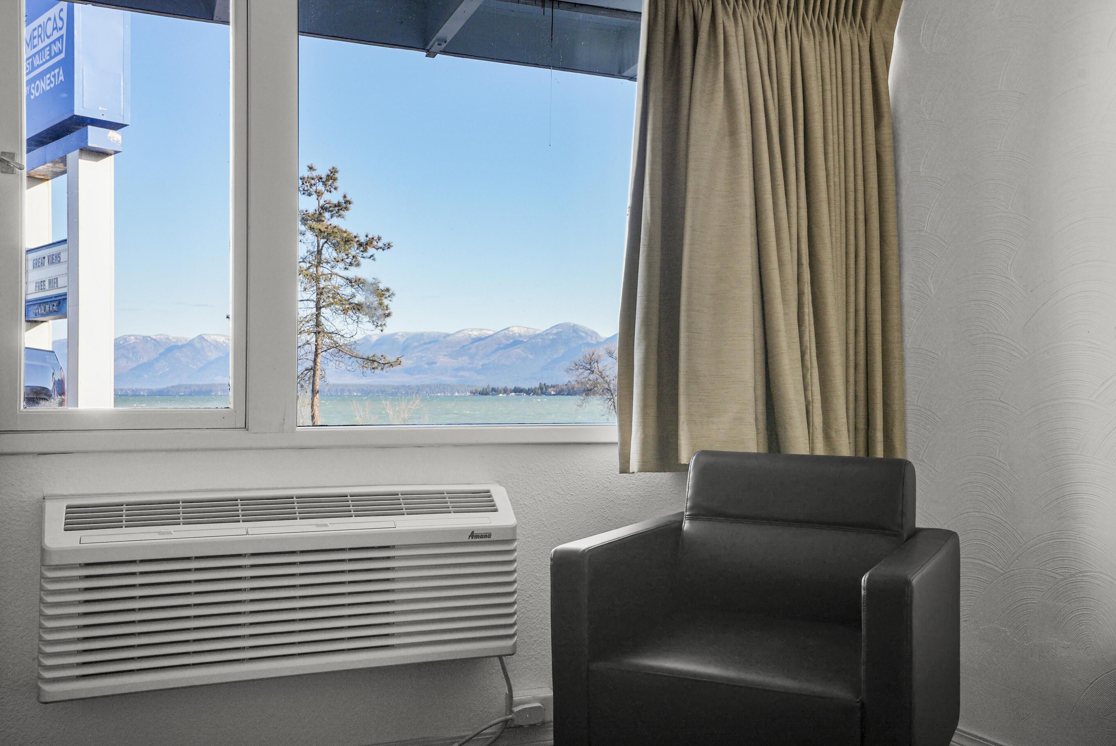 A room with a window, a black chair, and a white air conditioner.
