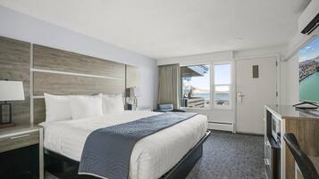 Een hotelkamer met een groot bed, een bureau met een computer, een televisie en uitzicht op zee.