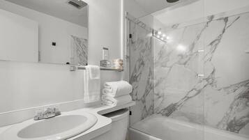 A modern bathroom with a marble shower, a sink, and a toilet.