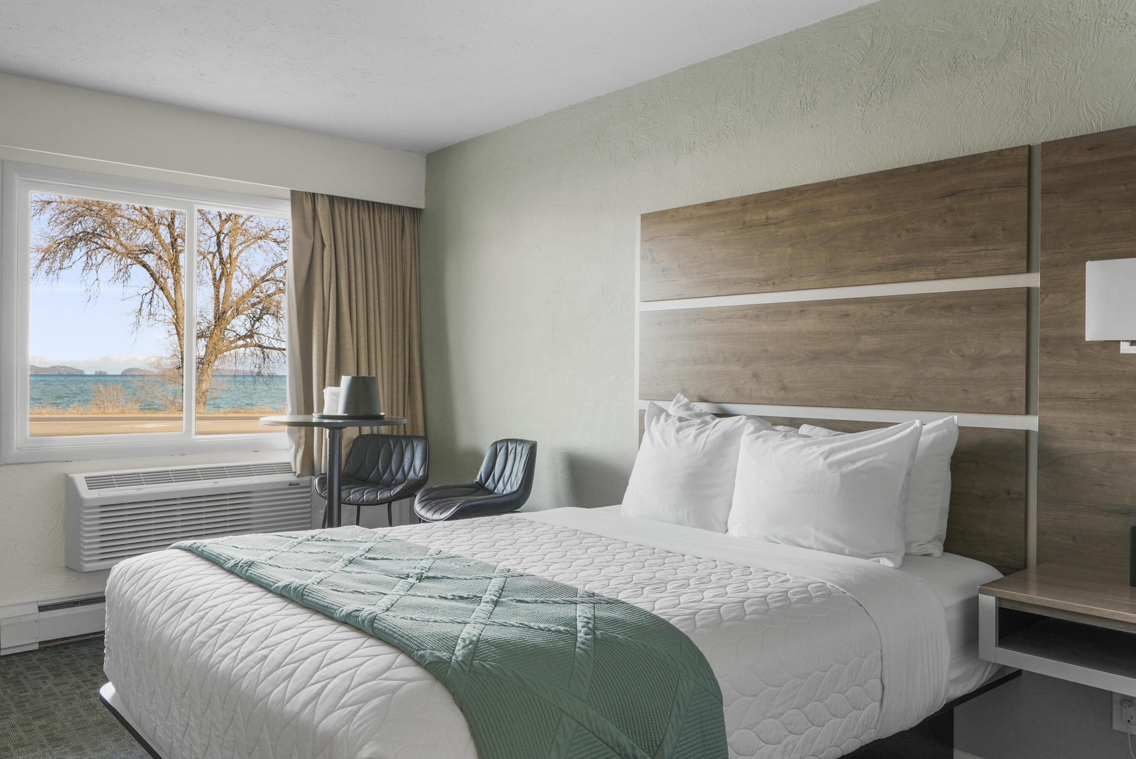 Een hotelkamer met een groot bed, uitzicht op zee, een stoel en een tafel met een lamp.