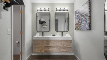 A bathroom with a double vanity, wooden cabinets, a large mirror, and a colorful artwork on the wall.