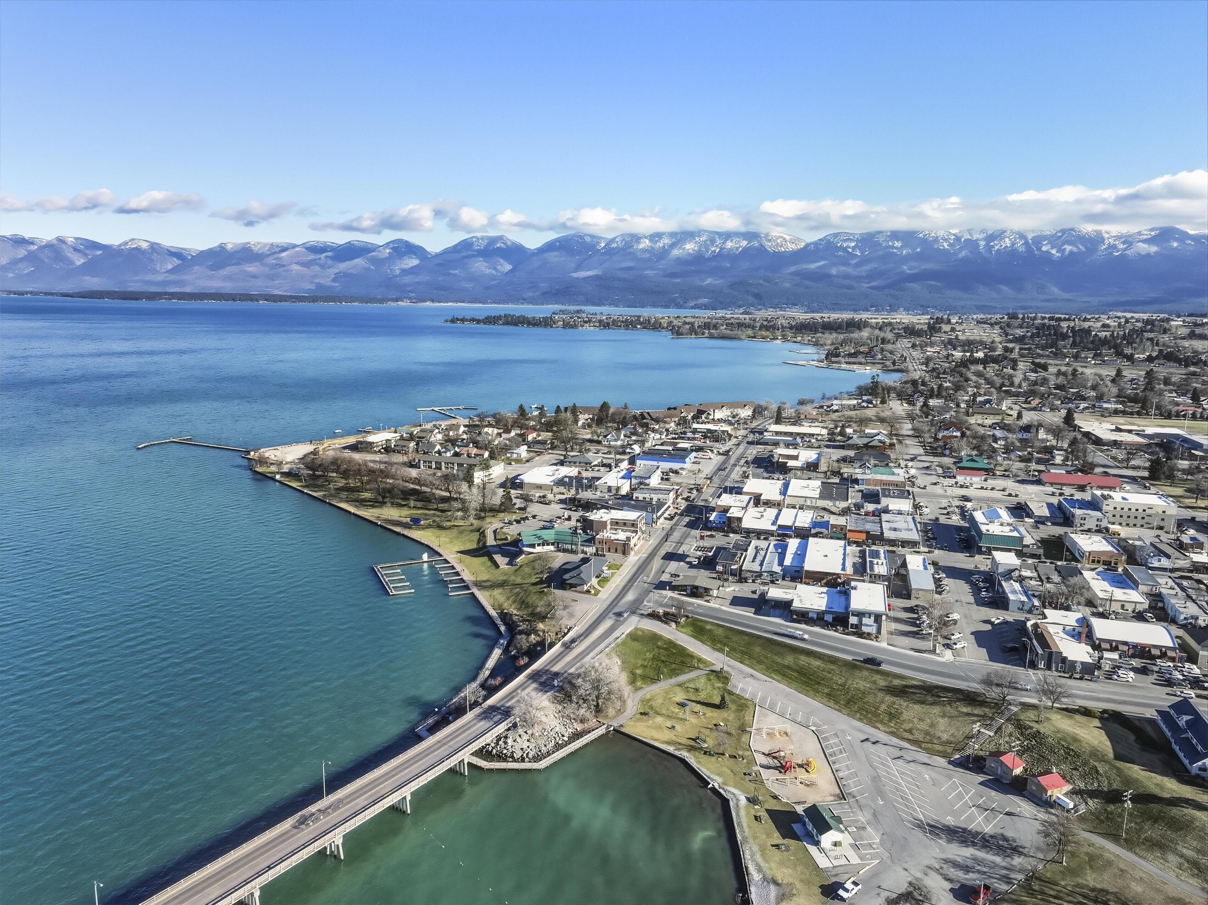 An aerial view of a coastal town with a marina, a bridge, and a mountain range in the background.