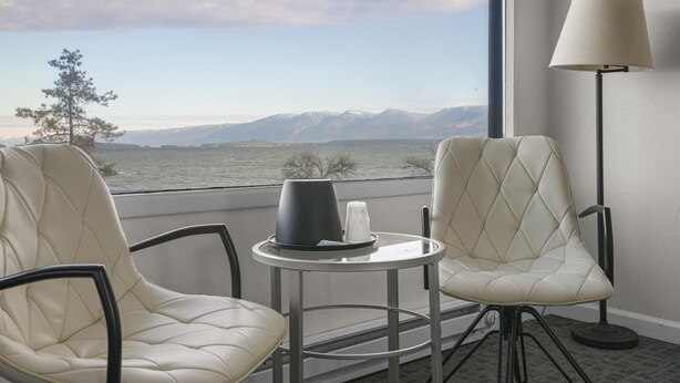 Habitación de hotel con dos sillones de cuero, una mesita con lámpara y vistas a montañas a través de amplios ventanales.